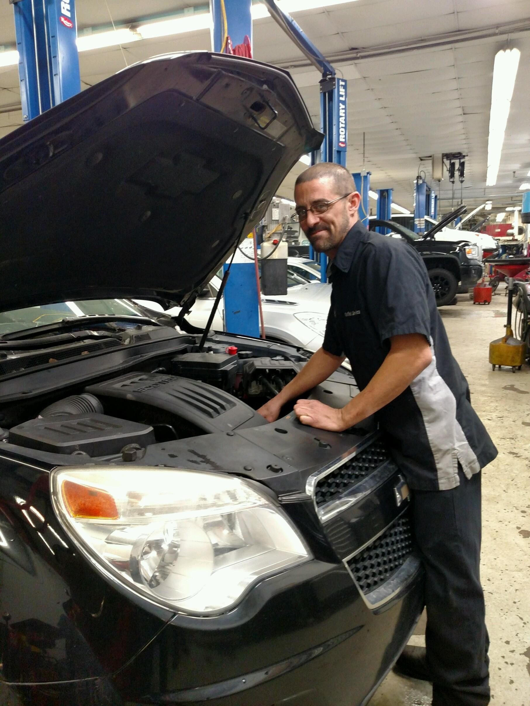 Technician working on a vehicle with hood open and hand in engine bay